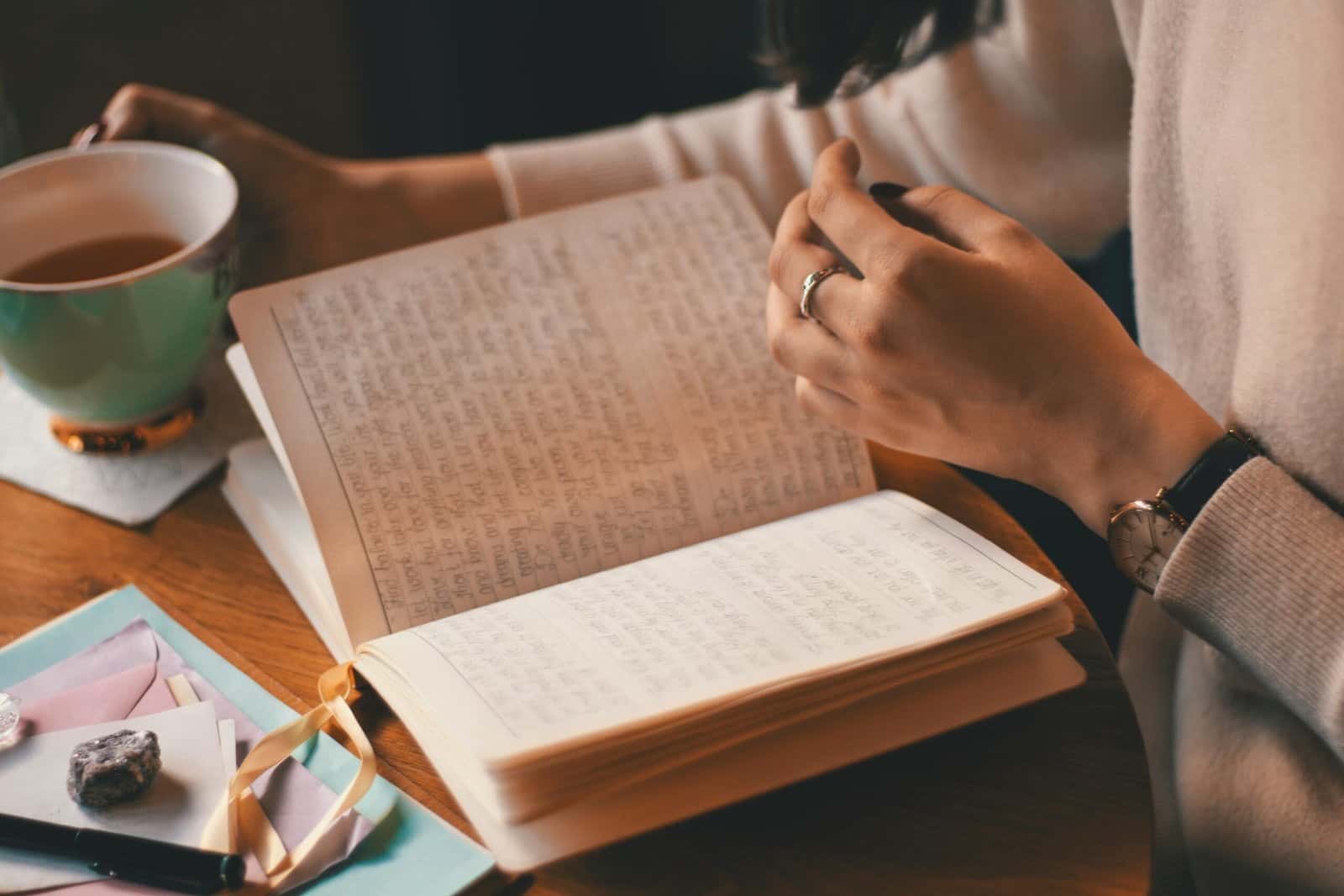 A woman writing in an open journal at a wooden table next to a cup of tea