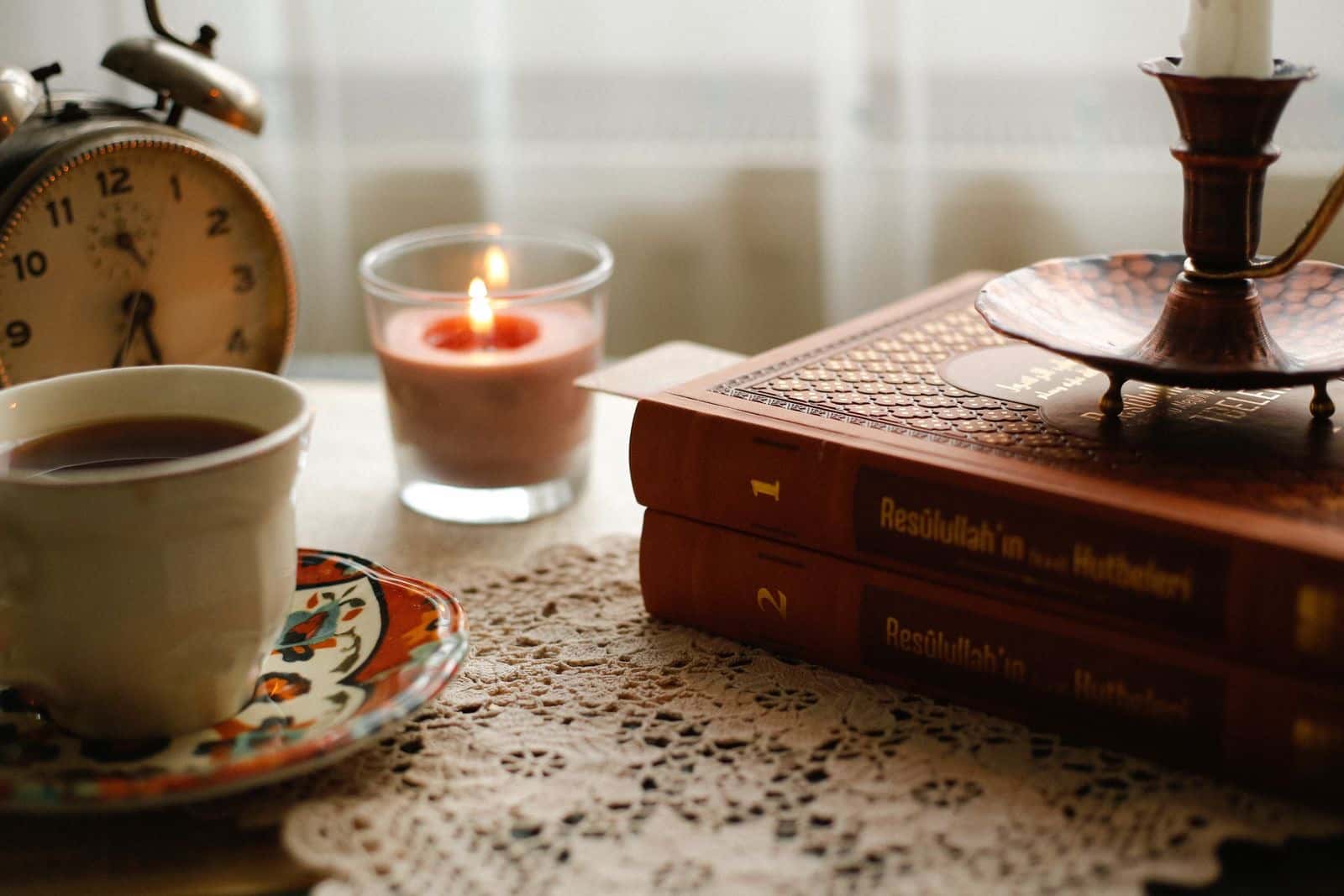 Old books, a cup of tea and a lit candle on a table
