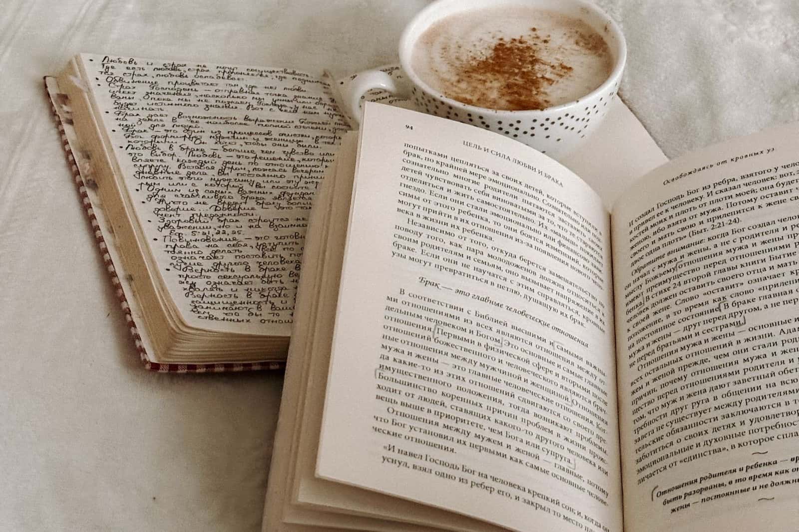 An open book and a journal beside a cup of coffee