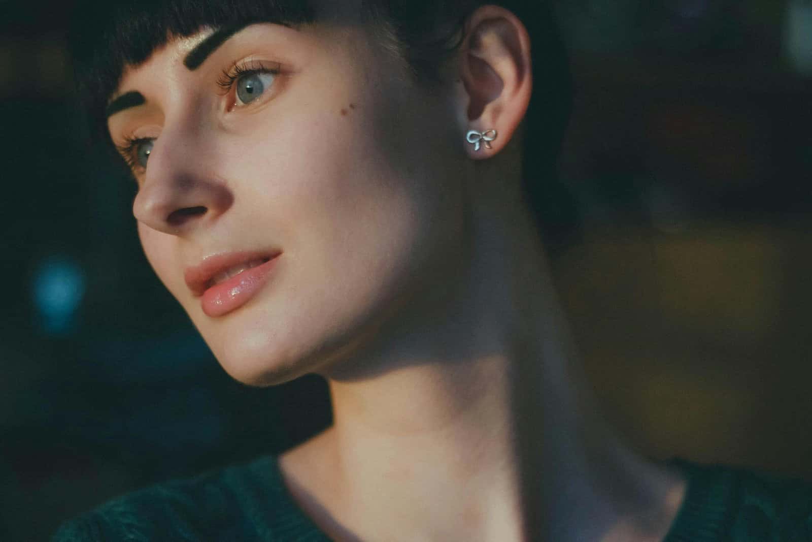 A young woman with short dark hair and a small earring looking to the side in soft evening light