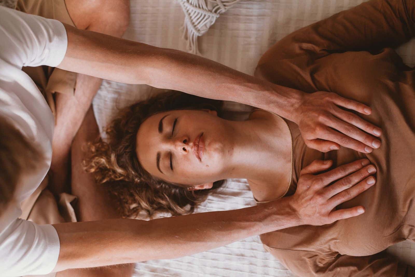 A woman lying with eyes closed while a practitioner rests hands gently on her