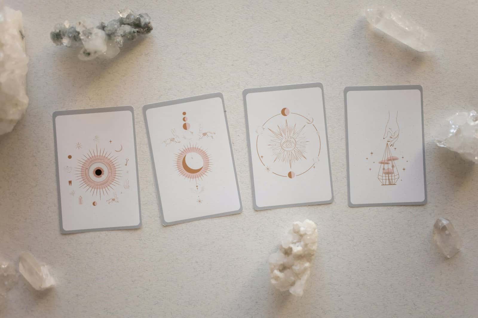 Four white oracle cards with sun and moon drawings laid out between clear quartz crystals