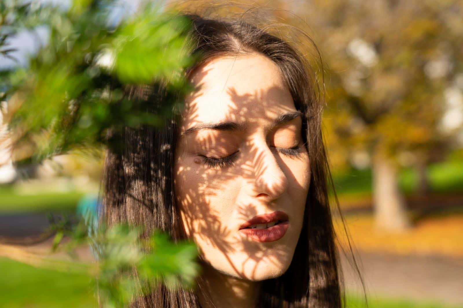 A woman with her eyes closed as sunlight and leaf shadows fall on her face