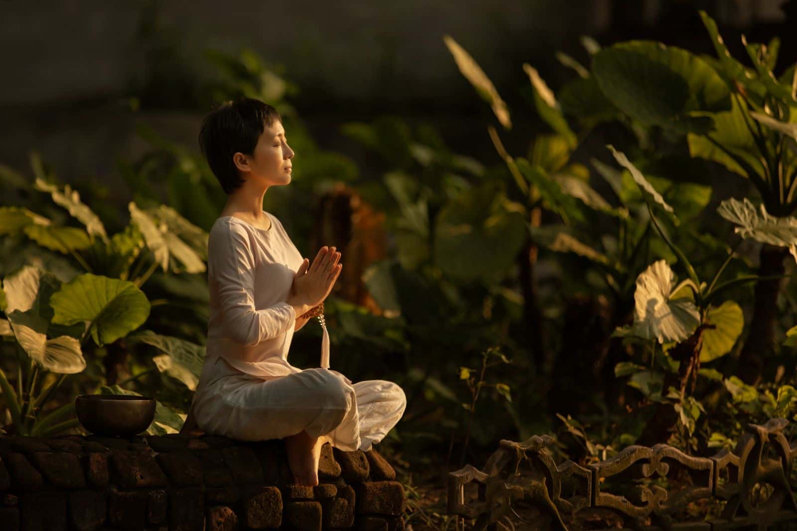 A woman meditating in a green garden with her hands together