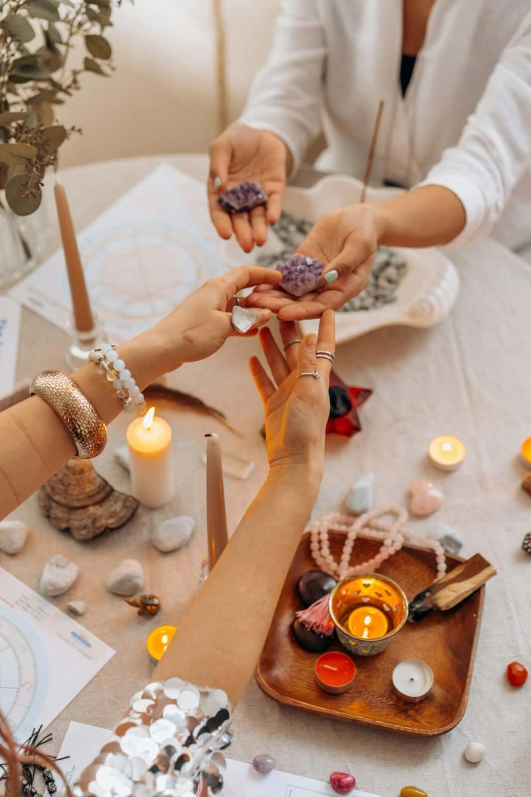Hands holding purple amethyst crystals over a table with candles, stones and an astrology chart
